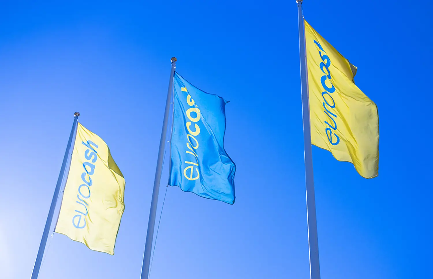 Eurocash-flaggor som vajar i vinden mot blå himmel.
