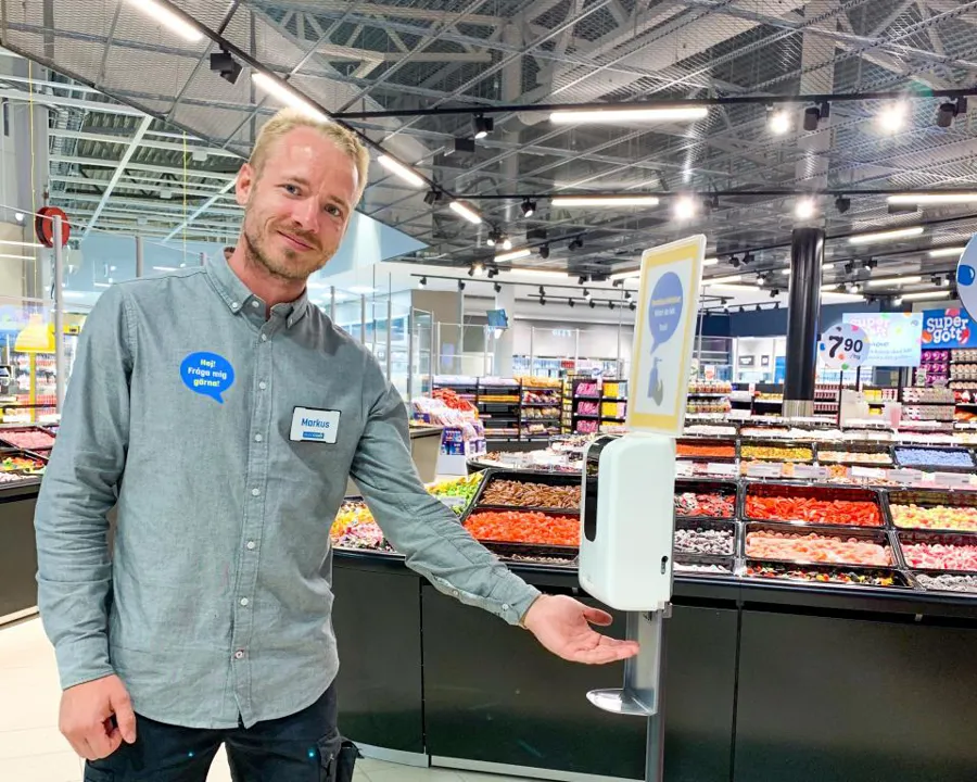 Butiksanställd står vid handspritsautomat